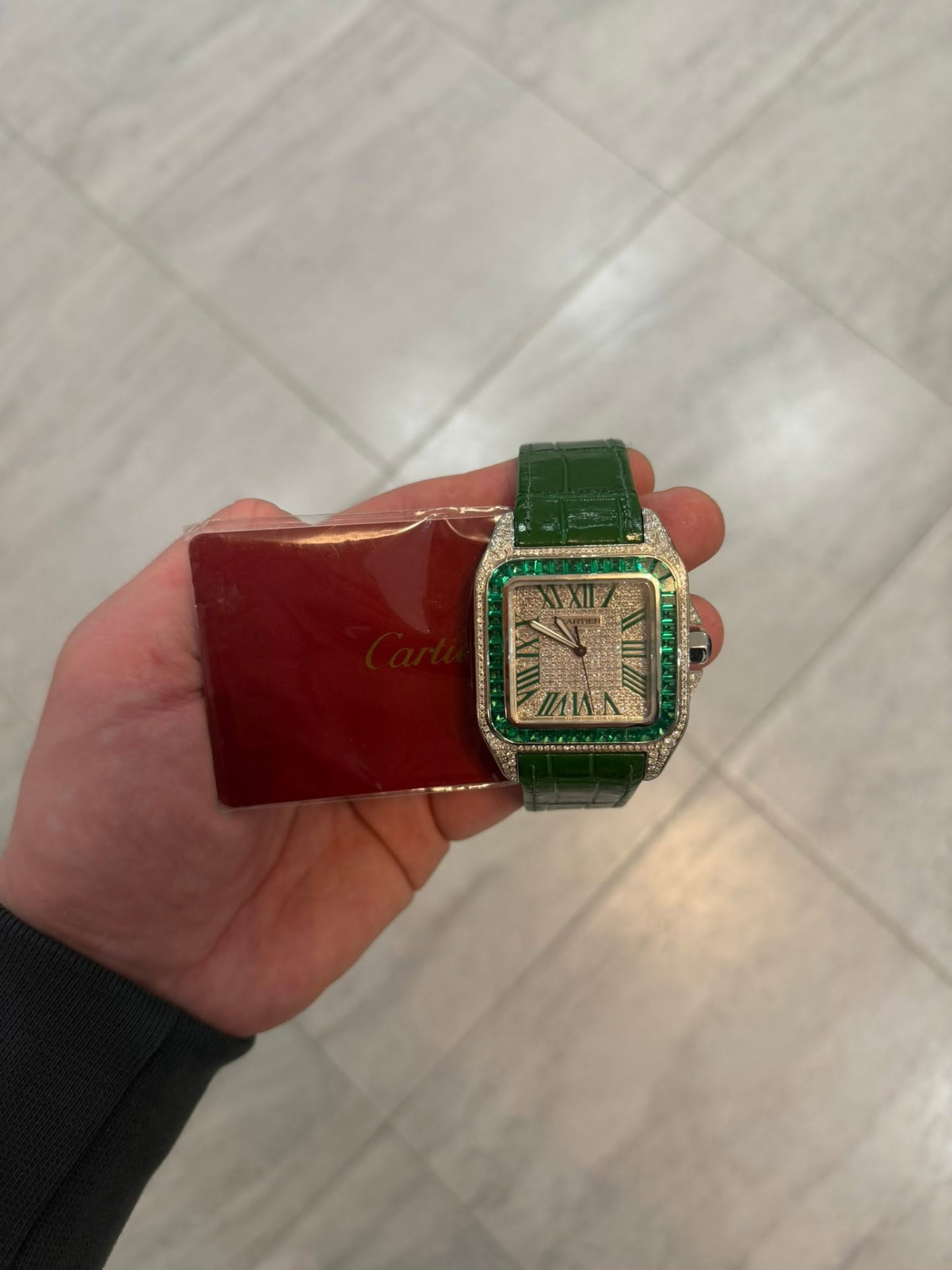 Diamond-set luxury watch with green stones and a green leather strap
