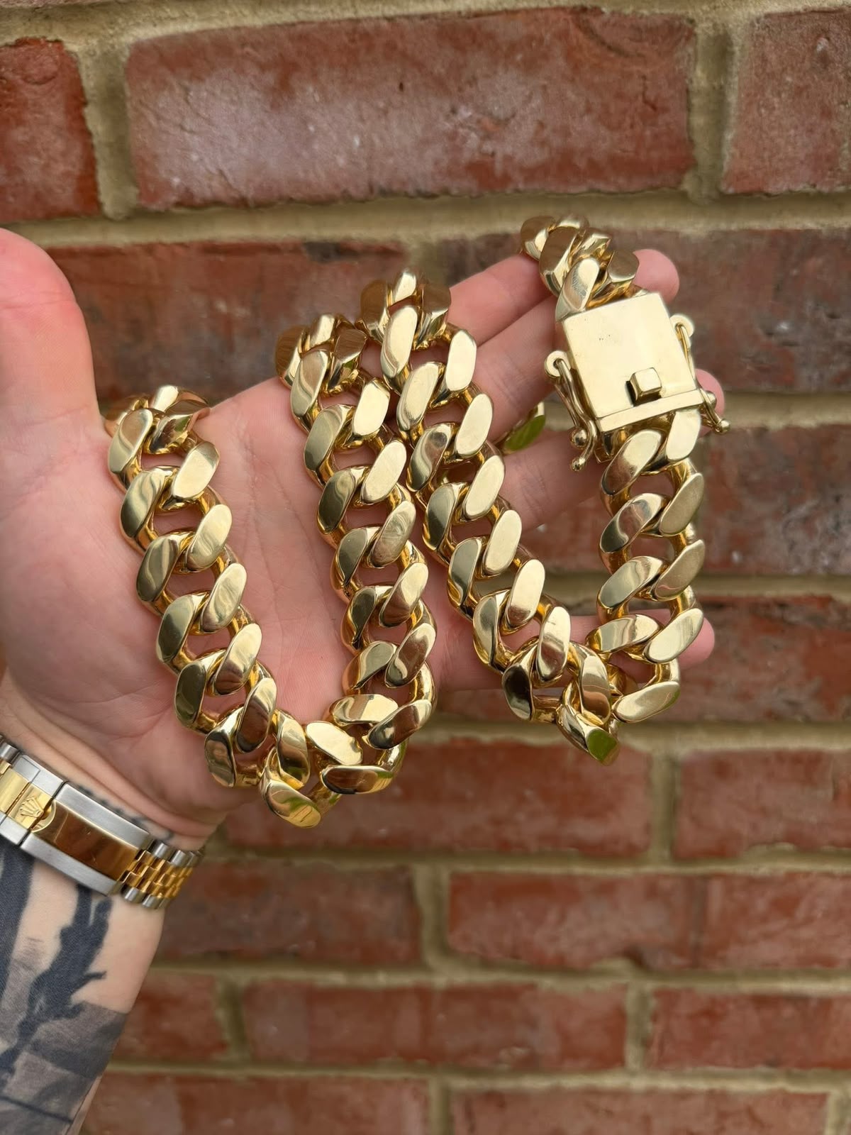 Heavy polished gold curb chain with a large box clasp held against a brick wall