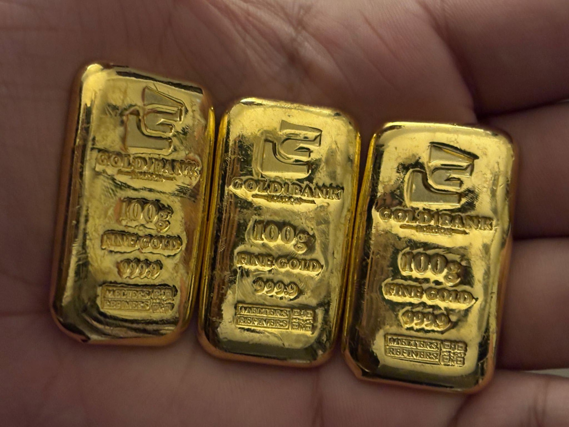 Three 100g fine gold 999.9 bullion bars held in a hand