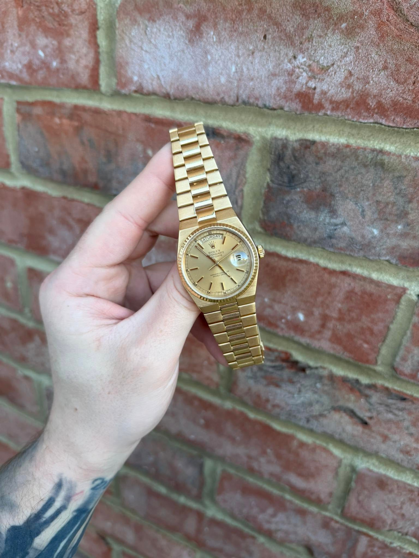 Gold day-date watch with a champagne dial held against a brick wall