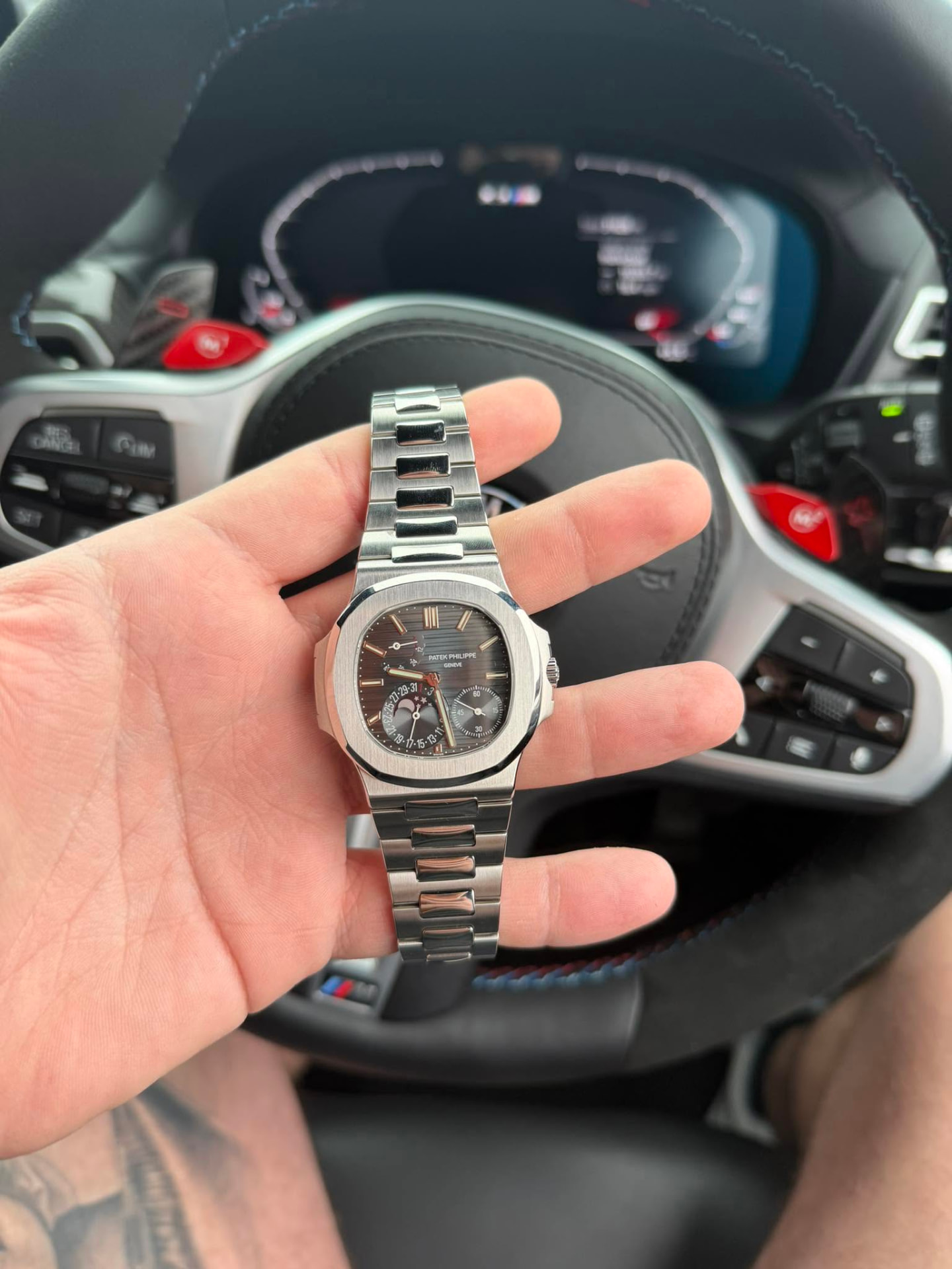 Steel luxury watch with a dark dial held inside a car