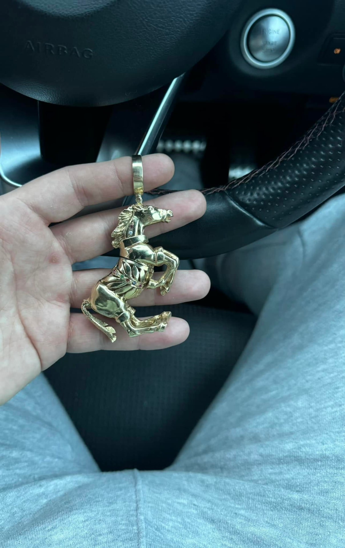Large solid gold rearing horse pendant held in a hand