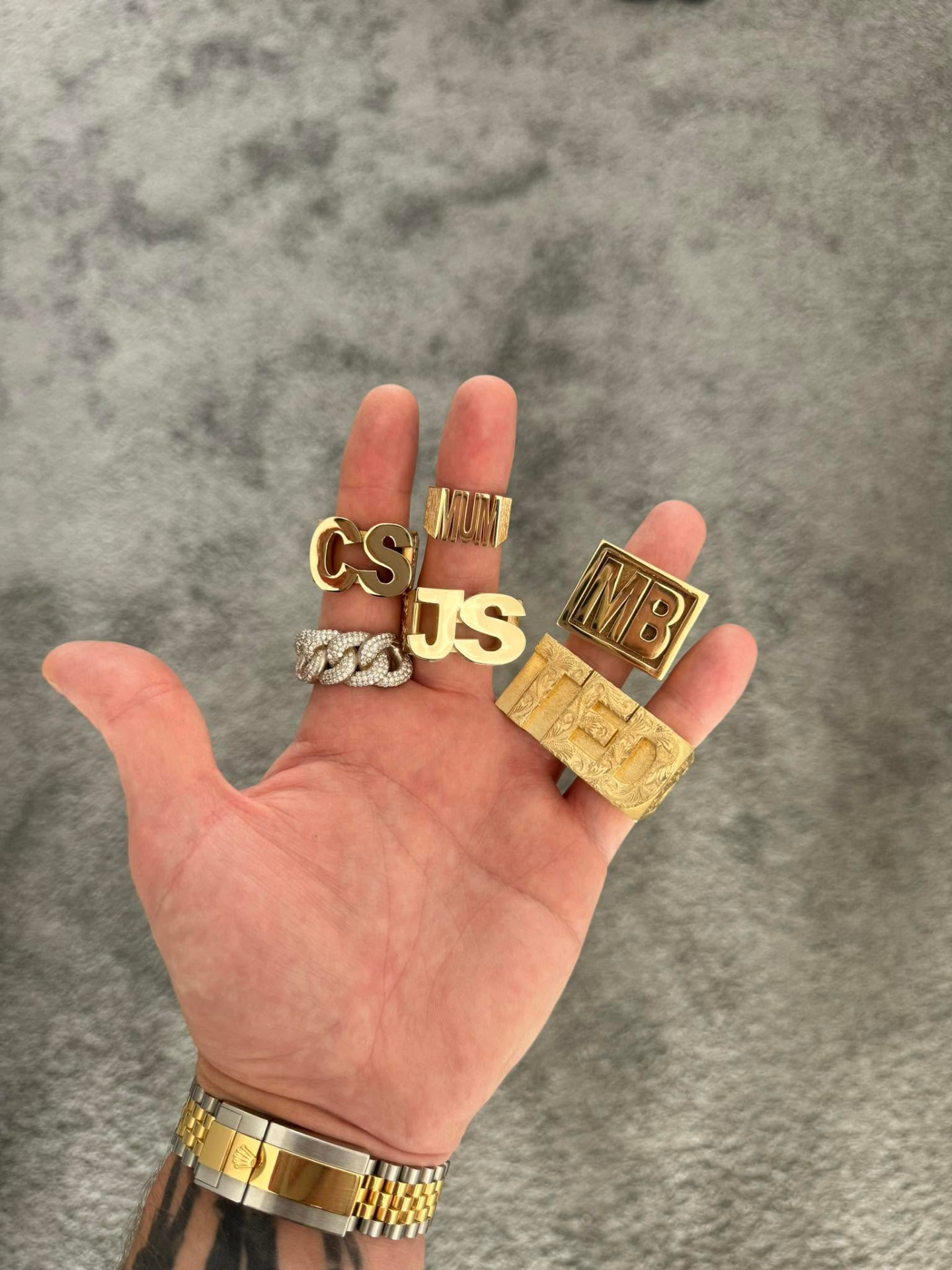 Hand holding custom gold initial rings, including CS, JS, MUM, MB and TED designs